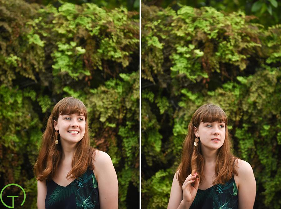A teenager poses near a wall of lush greenery at A high school senior poses amongst the bonsai tree collection at Matthaei Botanical Gardens for her ann arbor senior session